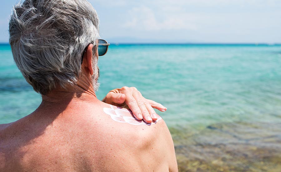 An elderly man applying sunscreen to his skin