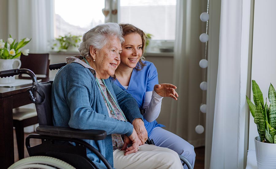 An elderly woman smiles with her nurse while looking out the window