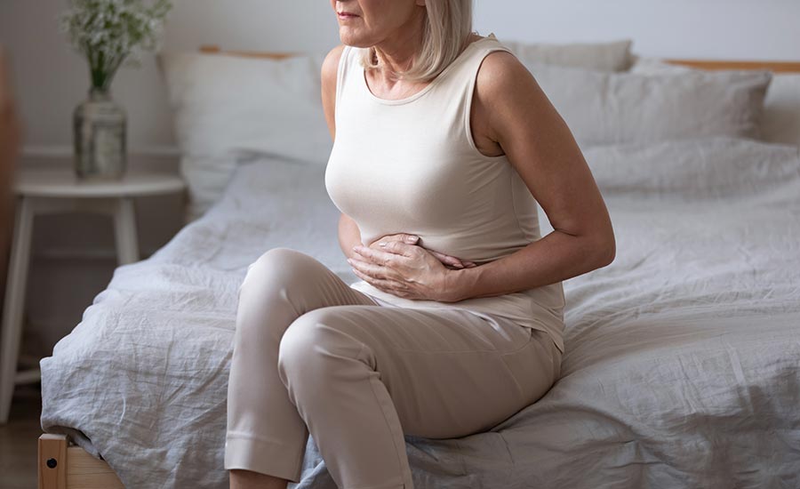 An elderly woman sitting on the bed while holding her stomach