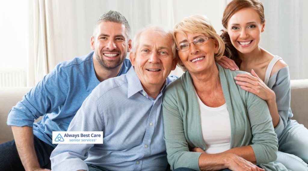 A family portrait with two adults and two seniors sitting together on a couch, smiling and enjoying each other’s company. The image features a caring family, representing the warmth and support of senior care