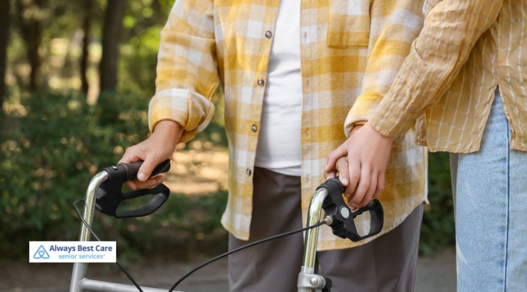 A close-up of a caregiver assisting a senior with a walker outdoors. The caregiver gently holds the senior's hand, ensuring they have the support needed for safe walking, emphasizing care and companionship.